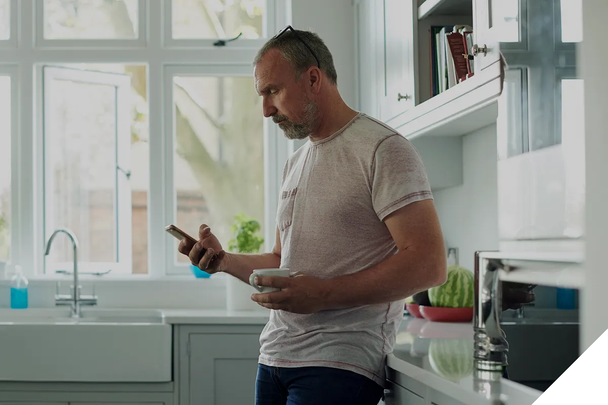 man using mobile phone in kitchen drinking tea